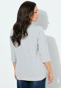 Top grigio chiaro con maniche a tre quarti, scollo rotondo e vestibilità comoda. Tessuto morbido e liscio, abbinato a jeans blu scuro.