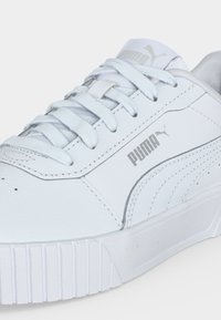 Baskets blanches Puma avec lacets blancs, logo sur le côté et semelle texturée, vues en gros plan de profil.