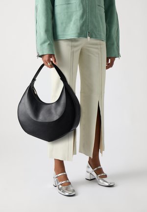 Fekete bőr kézitáska, félhold alakú, sima textúrával, krémszínű nadrággal és fémes ezüst cipővel párosítva.