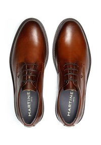 Chaussures habillées en cuir marron avec un bout rond, un laçage et une couture décorative le long du bord. Le logo à l'intérieur de la chaussure indique "MARTINE 1973."