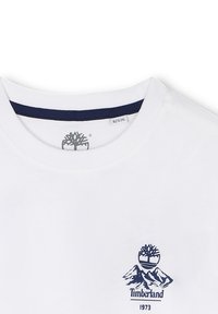 Witte Timberland t-shirt met ronde hals en marineblauwe kraagtrim en logo met een boom, bergen en de tekst "1973" op de borst.