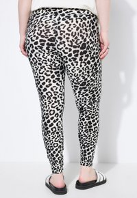 Zwart-witte leggings met luipaardprint, aansluitend ontwerp, rekbaar materiaal, soepel textuur, gecombineerd met zwart-witte slide sandalen.