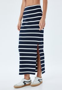 Marineblauwe en witte gestreepte maxi rok met een zijsplit, gemaakt van zachte stof. Gecombineerd met witte sneakers met grijze accenten.