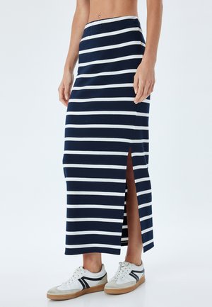 Gonna maxi a righe blu navy e bianche con uno spacchetto laterale, realizzata in tessuto morbido. Abbinata a sneaker bianche con dettagli grigi.