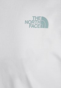 Vit bomullströja med en ljusblå logotyp för The North Face. Designen inkluderar en rundad ikon och text. Mjuk textur.