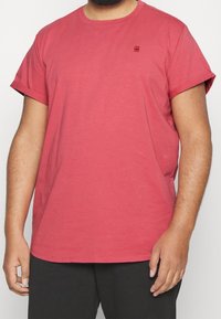 T-shirt en coton rouge avec des manches courtes, un col rond et un petit logo imprimé sur la poitrine. Présente une coupe décontractée.
