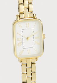 Gold rectangular watch with a white face, Roman numerals, and a textured link bracelet. Features a small crown on the side for adjustments.