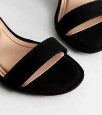 Sandalias de ante negro de punta abierta con una correa ancha sobre el pie y una suela con amortiguación baja, que presenta una plantilla beige lisa.