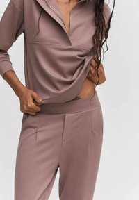 Top de cierre con cremallera en rosa claro, combinado con pantalones a juego. La tela parece suave con una textura blanda. Los pantalones tienen bolsillos frontales y ligeros pliegues.