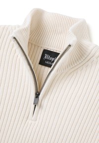 Pullover a coste color crema con colletto alto con zip. Presenta un motivo testurizzato e un'etichetta del marchio nera all'interno del colletto.