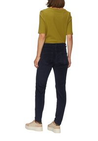 Olijfgroene geribbelde top met korte mouwen, gecombineerd met donkerblauwe corduroypantalon en beige platform sneakers. Zichtbare achterzakken op de broek.