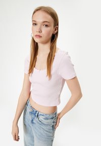 Lichtroze geribde crop top met korte mouwen en geschulpte kanten rand rond de halslijn. Gecombineerd met lichtblauwe loszittende jeans.