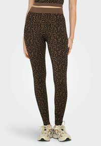 Brązowe legginsy w cętki z prążkowaną strukturą i wysokim stanem, w połączeniu z jasnymi sneakersami.