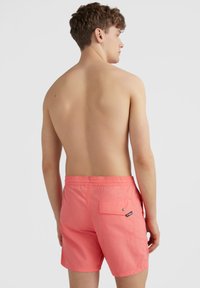Shorts de bain corail avec taille élastique, poches latérales et arrière, et une petite étiquette logo sur la poche arrière. Matériau lisse et léger.