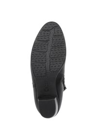 Schwarze Schuhsohle mit einem strukturierten Muster für Grip, versehen mit einem erhabenen Logo. Glatte Kanten und eine leichte Krümmung an den Zehen.