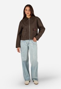 Pruun lühike jakki, millel on eest tõmblukk, kaks suurt klapptaskut ja kraega kaelus, mida on kaasas helesinised flared teksad.