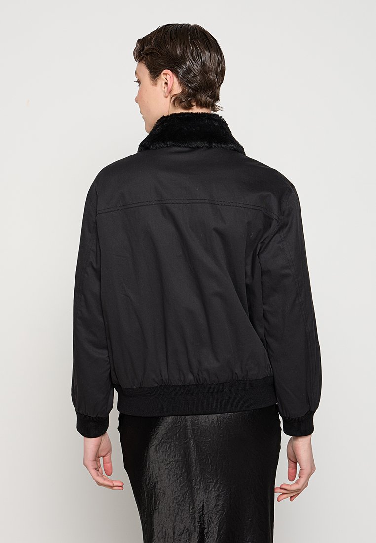 Czarna kurtka bomber z futrzanym kołnierzem, elastycznymi mankietami i dołem oraz gładką fakturą materiału. Posiada luźny krój i minimalistyczny design.