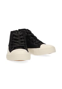 Zapatillas altas de tela negra con un upper texturizado, puntera de goma crema y cordones negros. Presenta detalles metálicos en la tela.