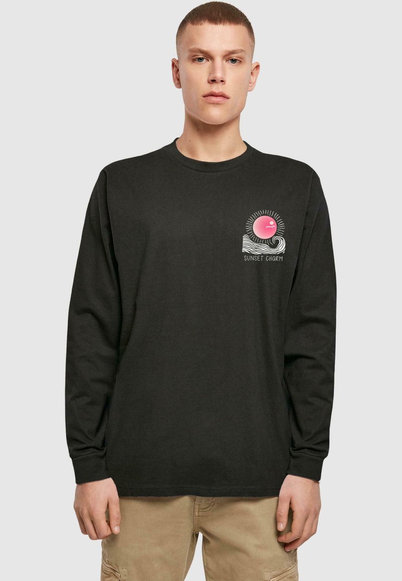 Tricou cu mânecă lungă negru, decorat cu un grafic al unui soare roz cu raze, plasat pe un fundal cu un design de valuri albe și textul "CHARMUL APUSULUI". Material din bumbac.