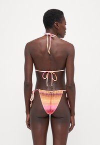 Le ensemble de bikini présente un dégradé d'orange et de rose avec des liens ajustables. Le haut est de style triangle ; le bas a des liens sur les côtés et une coupe basse.