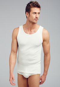 Vit ribbad tanktop med rund halsringning och figurnära design, kombinerad med matchande figurnära underkläder. Slät textur utan synliga mönster.