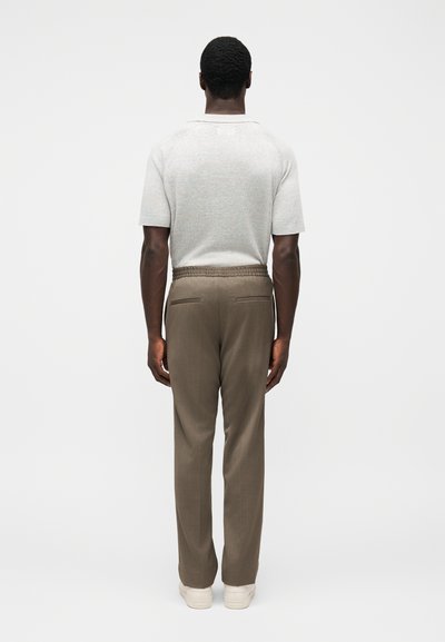 Ανοιχτό γκρι πλεκτό πουκάμισο με κοντά μανίκια σε συνδυασμό με καφέ παντελόνια με κορδόνι στη μέση και πλαϊνές τσέπες, φορεμένο με λευκά αθλητικά παπούτσια.