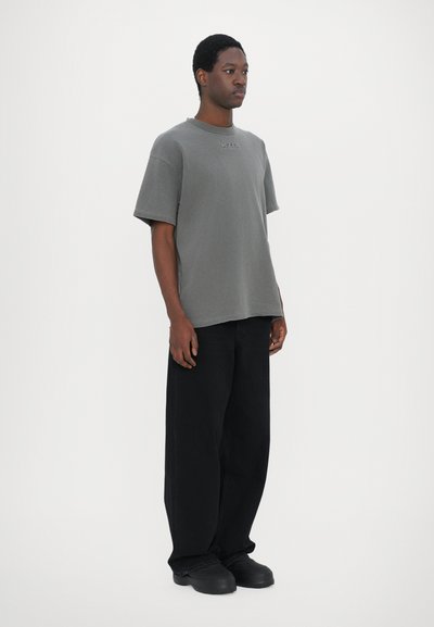 T-shirt gris à manches courtes avec un col rond, associé à un pantalon noir ample et des chaussures noires simples.