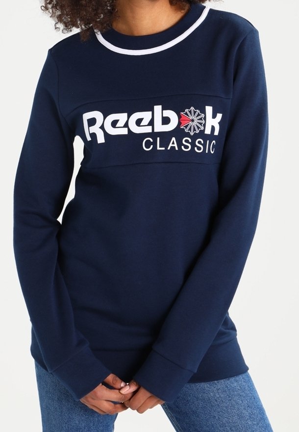 Mörkblå sweatshirt med vit halsringning och Reebok Classic-logotyp. Har långa ärmar och en avslappnad passform. Mjukt material och minimal design.