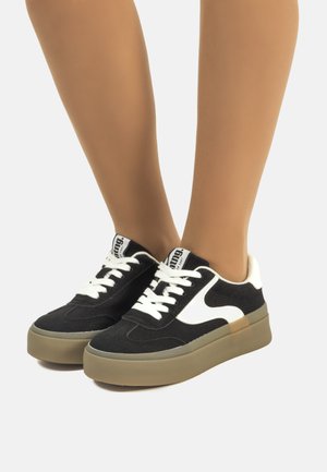 Baskets noir et blanc avec un tissu texturé, bout rond, semelle épaisse beige et lacets blancs. Présente un logo sur la languette et des accents sur le côté.