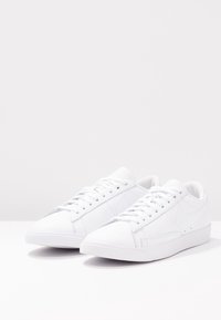 White sneakers with a smooth leather exterior, flat laces, a rounded toe, and minimalist design featuring a subtle logo.