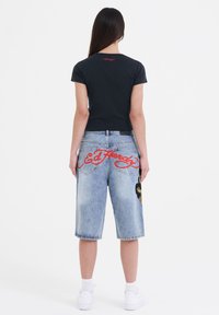 Black cropped t-shirt with red lettering, paired with light blue denim shorts featuring a large embroidered design and cuffed hems.