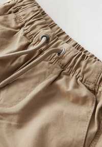 Pantaloni corti beige realizzati in tessuto misto cotone, con una vita elastica dotata di coulisse e dettagli cuciti sulle tasche.
