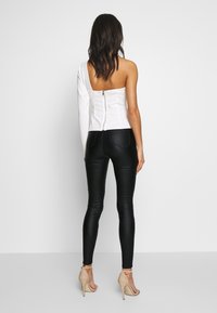 Vit enaxlad topp med dragkedja bak, kombinerad med svarta tajta byxor. Toppen har en slät yta, medan byxorna har en elegant finish.