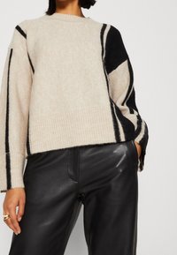 Beige svetr z vlněné směsi s černým geometrickým vzorem, žebrovaným lemem a manžetami, oversized střih, doplněný černými koženými kalhotami. Měkká textura.