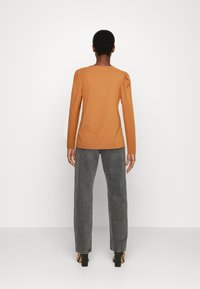 Blusa de manga longa em tecido laranja canelado com ombros bufantes, combinada com jeans cinzentos de cintura alta e sapatos pretos de salto quadrado.