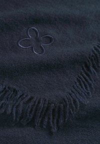 Donkerblauwe dekentje met een zachte textuur, franjes aan de randen en een bloemmotief in reliëf. Materiaal lijkt warm en knus.