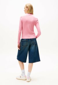 Figurbetontes pinkes Langarmoberteil kombiniert mit weiten blauen Denim-Culottes. Das Model trägt weiße Sneaker mit pinken Akzenten und weiße Socken.