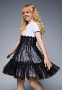 Rochie din tul negru cu un corset ajustat și un fustă stratificată. Cămașă albă cu mânecă scurtă dedesubt cu text. Textură netedă, aspect semi-transparent.