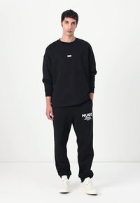 Black sweatshirt and jogger set made of cotton. Sweatshirt features a small labeled patch; joggers display a white logo on the left leg.