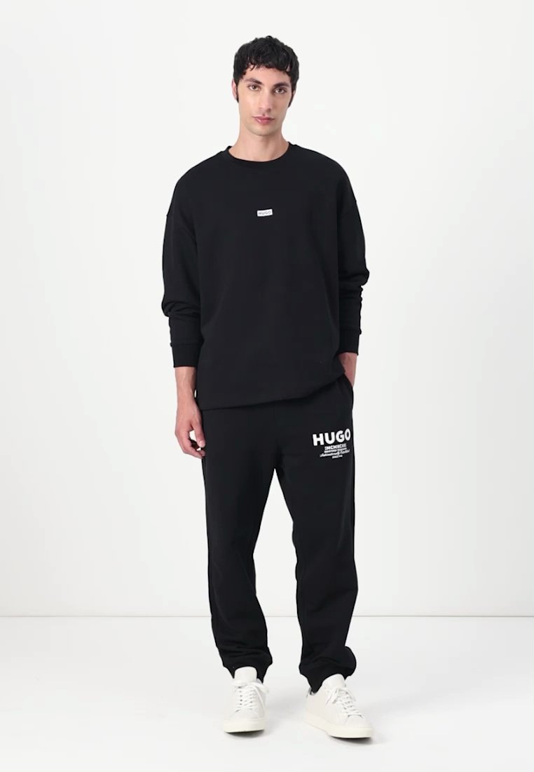 Ensemble sweat-shirt et pantalon de jogging en coton. Le sweat-shirt comporte une petite étiquette; le pantalon de jogging affiche un logo blanc sur la jambe gauche.