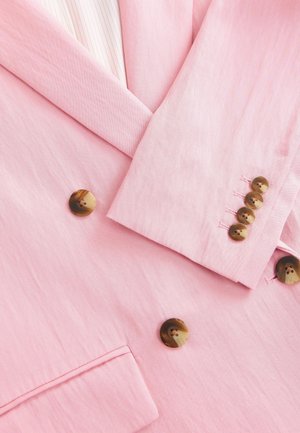 Růžový blejzr s texturovanou látkou, s výstřihem do "V", čtyřmi zaoblenými hnědými knoflíky a viditelnými švy.