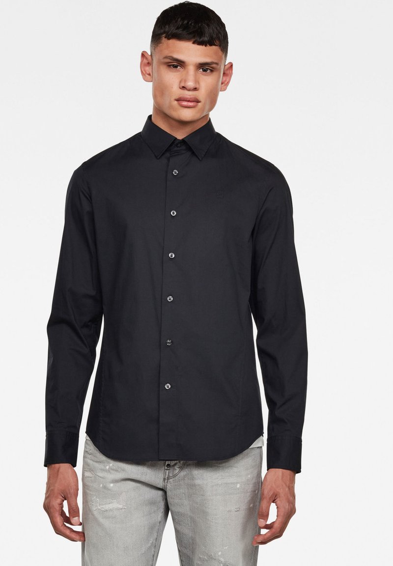 Camicia nera a maniche lunghe con colletto, caratterizzata da una vestibilità slim, chiusura anteriore con bottoni e un sottile logo sul petto.