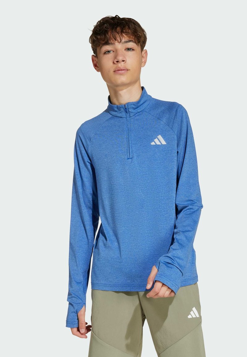 Modrý atletický top s dlhým rukávom a polovými zipsami, s textúrovanou tkaninou a bielym logom na ľavej hrudi. Jednoduchý dizajn.