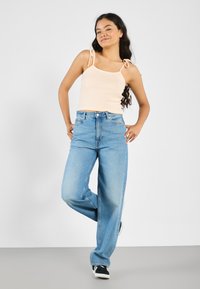 Lys ferskenfarvet ribbet crop top med bindebånd parret med højtaljede, løstsiddende lysblå jeans. Sorte sneakers fuldender outfittet.