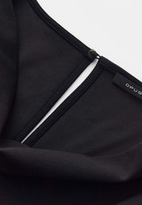 Close-up of a black garment neckline with a small black button loop closure and a fabric brand tag labeled "OPUS."
