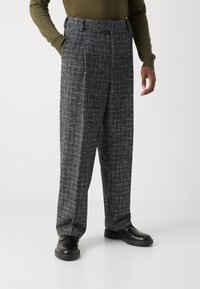 Pantaloni din amestec de lână cu un model în carouri, talie înaltă, croi lejer, scheme de culori alb-negru și buzunare laterale. Purtați cu pantofi negri.
