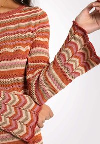 Pull en tricot avec des motifs en chevron multicolores dans des teintes d'orange, de rose et de beige. Manches évasées et col rond.