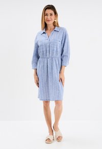 Blau gestreifter Kleid mit Kragen, Knopfleiste und elastischem Bund. Dreiviertelärmel und eine Brusttasche. Getragen mit leichten Espadrilles.