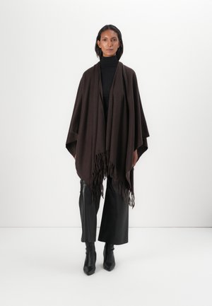 Bruine poncho met een textuur gebreid, voorzien van een franjerand. Gestyled met een zwarte coltrui, zwarte wijde broek en zwarte puntige laarzen.