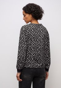 Maglione nero con motivo astratto bianco, polsini e colletto a coste. Maniche lunghe, vestibilità rilassata e orlo dritto sul retro.